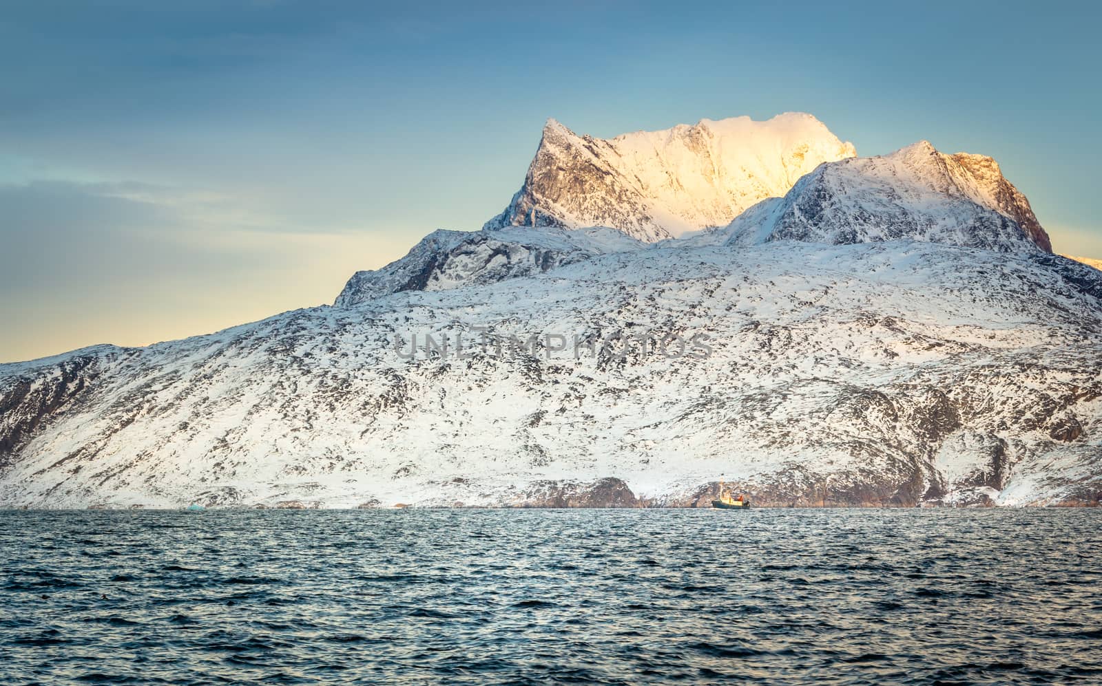 Huge Sermitsiaq mountain covered in snow with blue sea and small fishing boat, nearby Nuuk city, Greenland