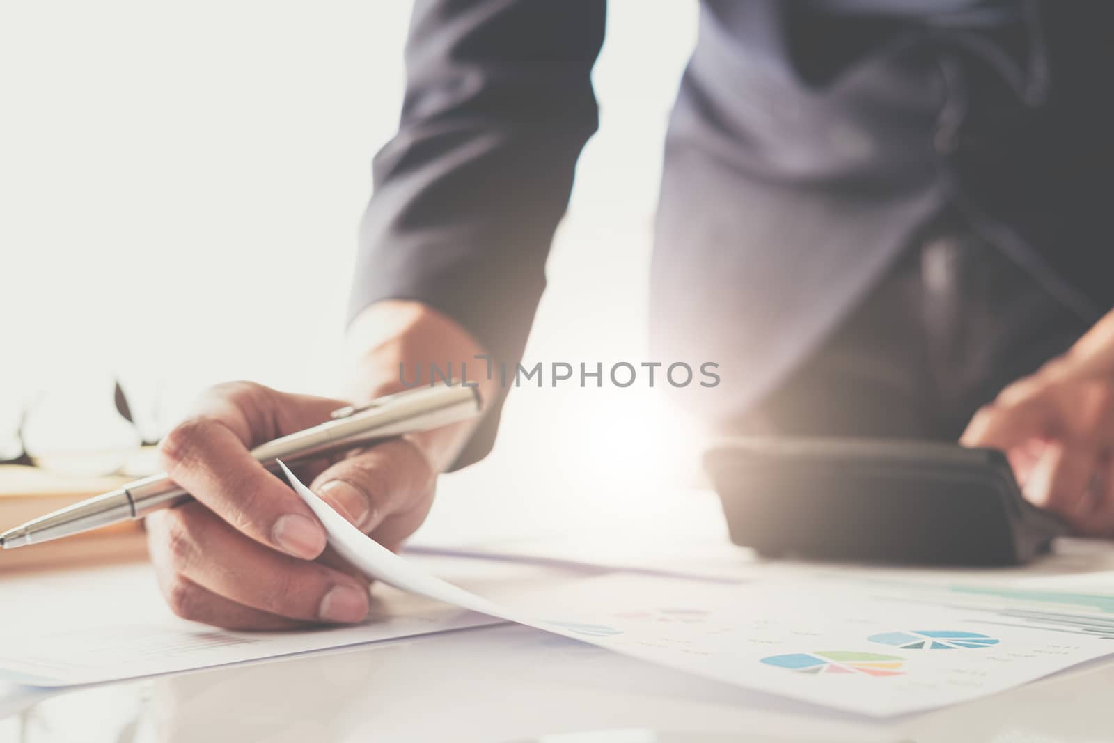Close up of businessman or accountant hand holding pen working on calculator to calculate business data, accountancy document and laptop computer at office, business concept