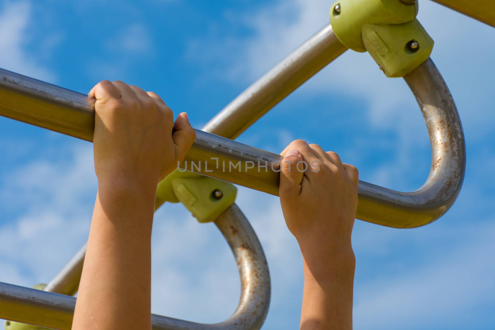 Two child's hand grabbing monkey bars at a playground conecept h by kingmaphotos