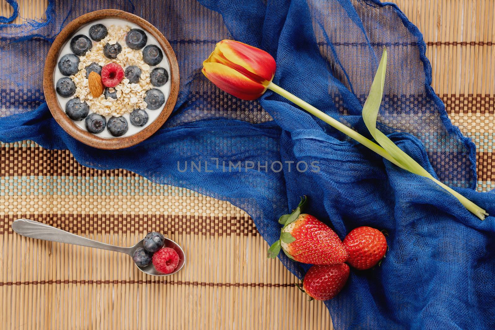 Valentine's Breakfast. Bowl of oatmeal with fruit on wooden tablecloth with tulip and blue scarf.