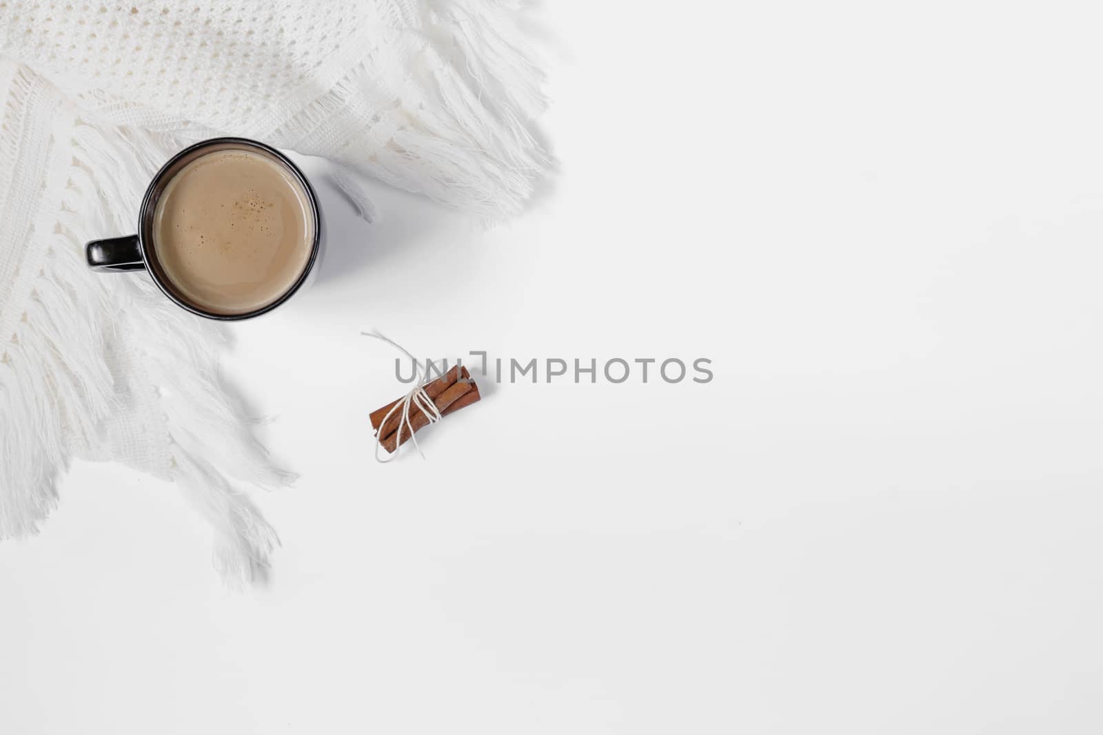 Black cup of white coffee with cinnamon and white crocheted scarf on a white background. View from above.