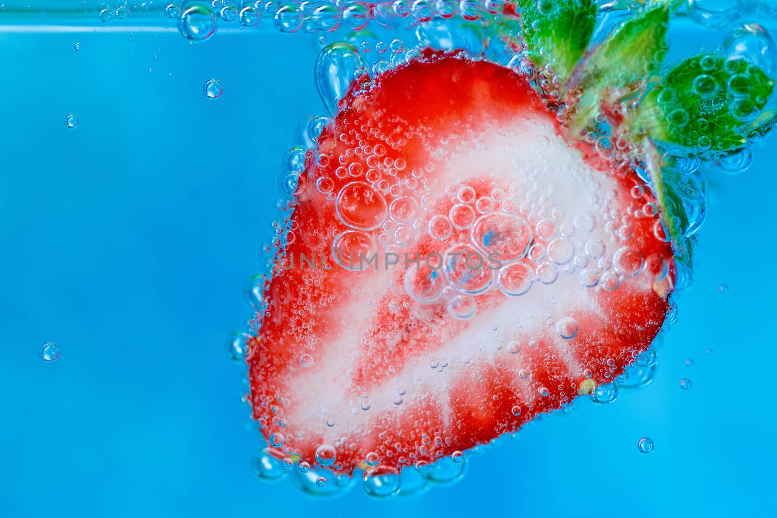 slice of strawberry in a glass of water on a blue background with bubbles