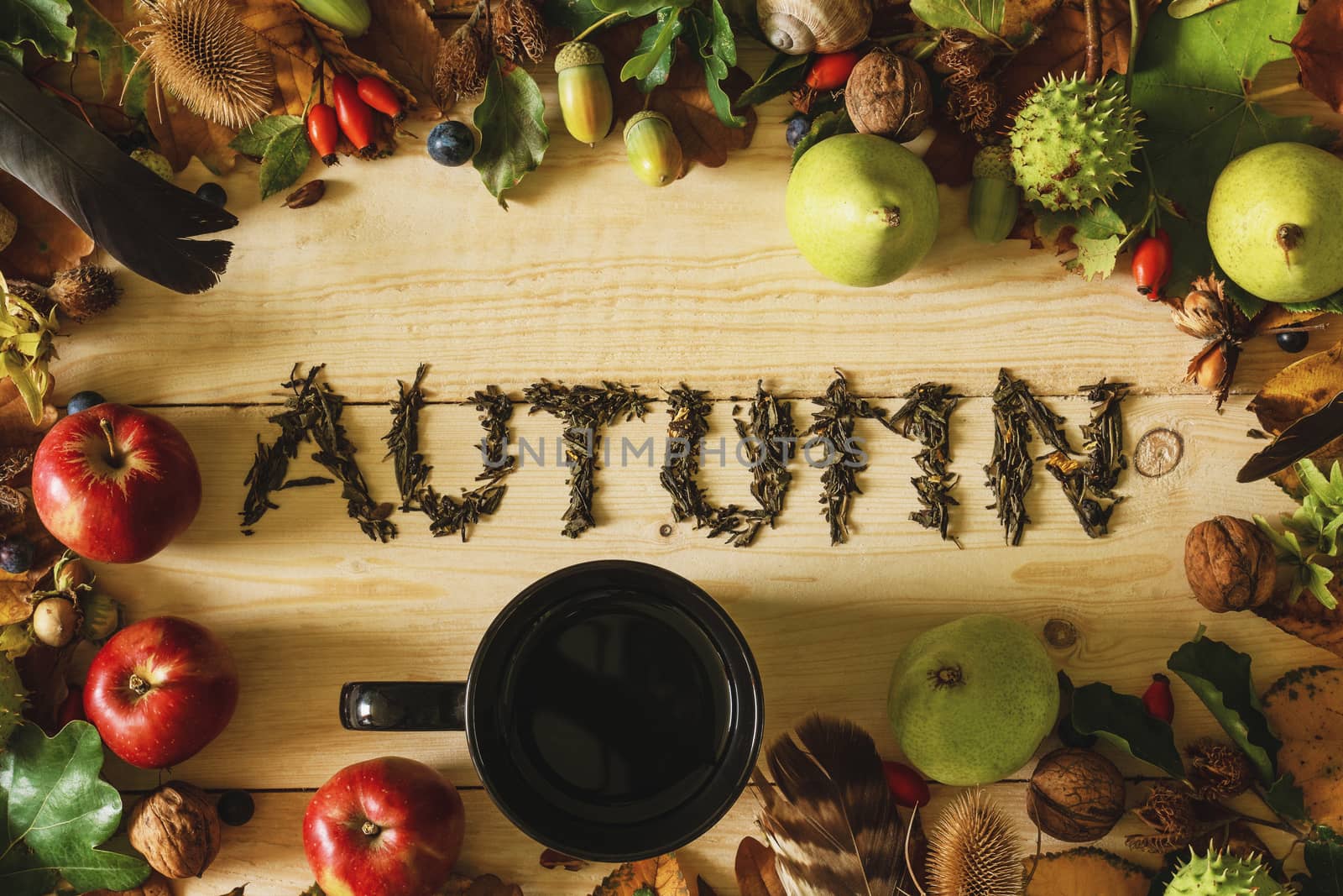 Autumn concept. A black cup of tea on a wooden table with a frame of autumn crops and falling leaves.