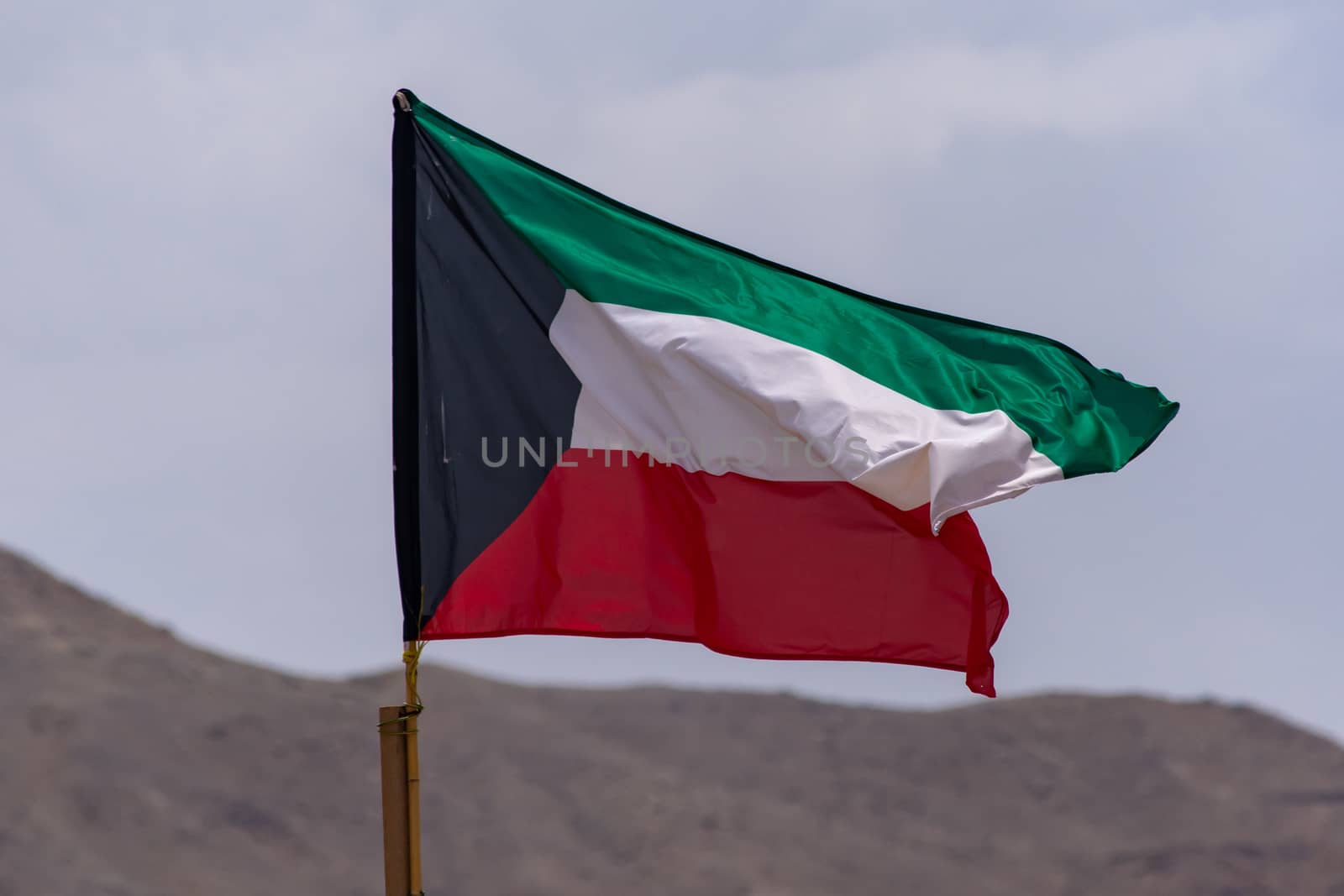 Kuwait Flag flying and waving in the sunshine with a blue sky and mountainous background.