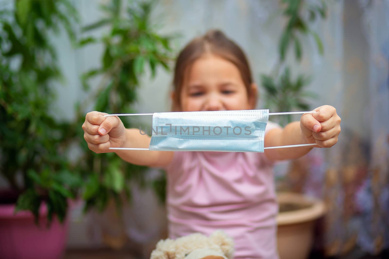 Little girl holds a medical mask in outstretched hands. The child puts on a protective mask