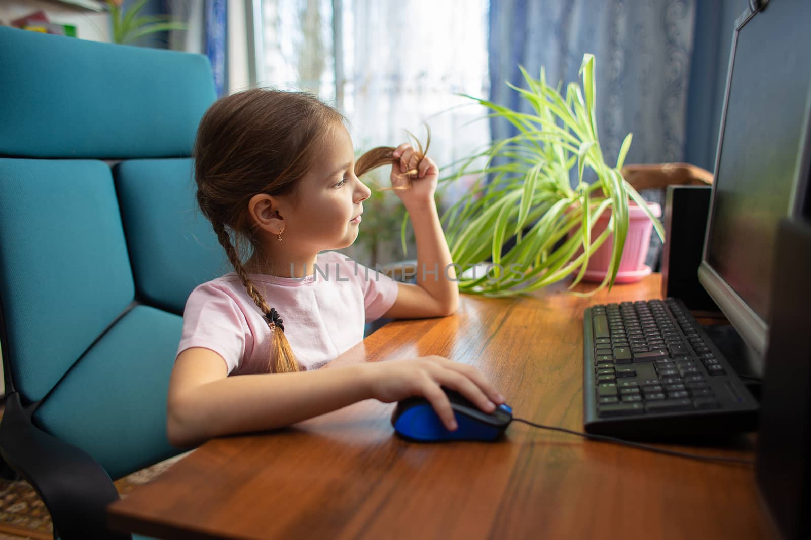 Girl schoolgirl with pigtails sits at home in an armchair at a desktop computer and drives a computer mouse