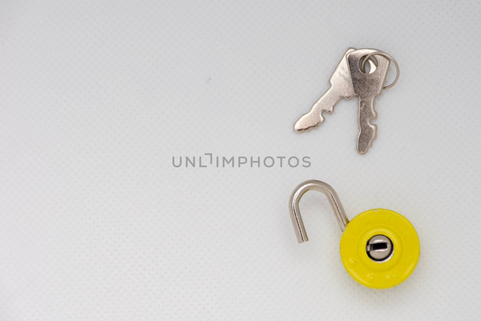 Silver keys and a yellow unlocked padlock on an isolated white b by kingmaphotos