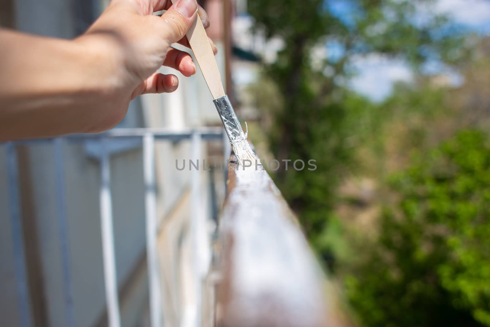 The process of painting rusty peeling rods on the fence. Man paints a brush with a fence, hand closeup. Spring work or repair