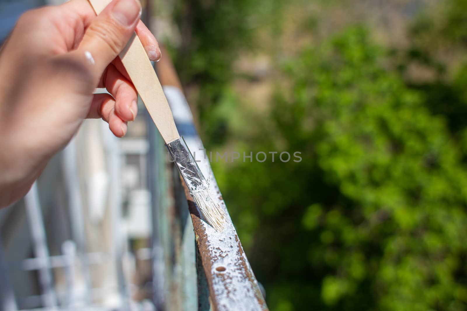 The process of painting rusty peeling rods on the fence. Man paints a brush with a fence, hand closeup. Spring work or repair