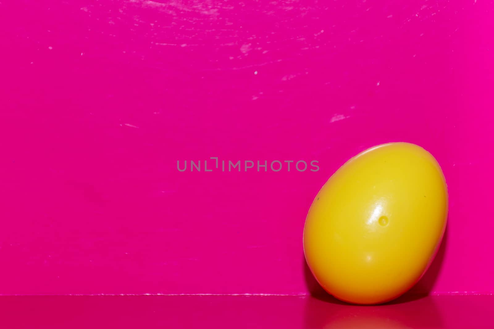 Yellow plastic egg in bottom right corner of a deep bright pink  by kingmaphotos