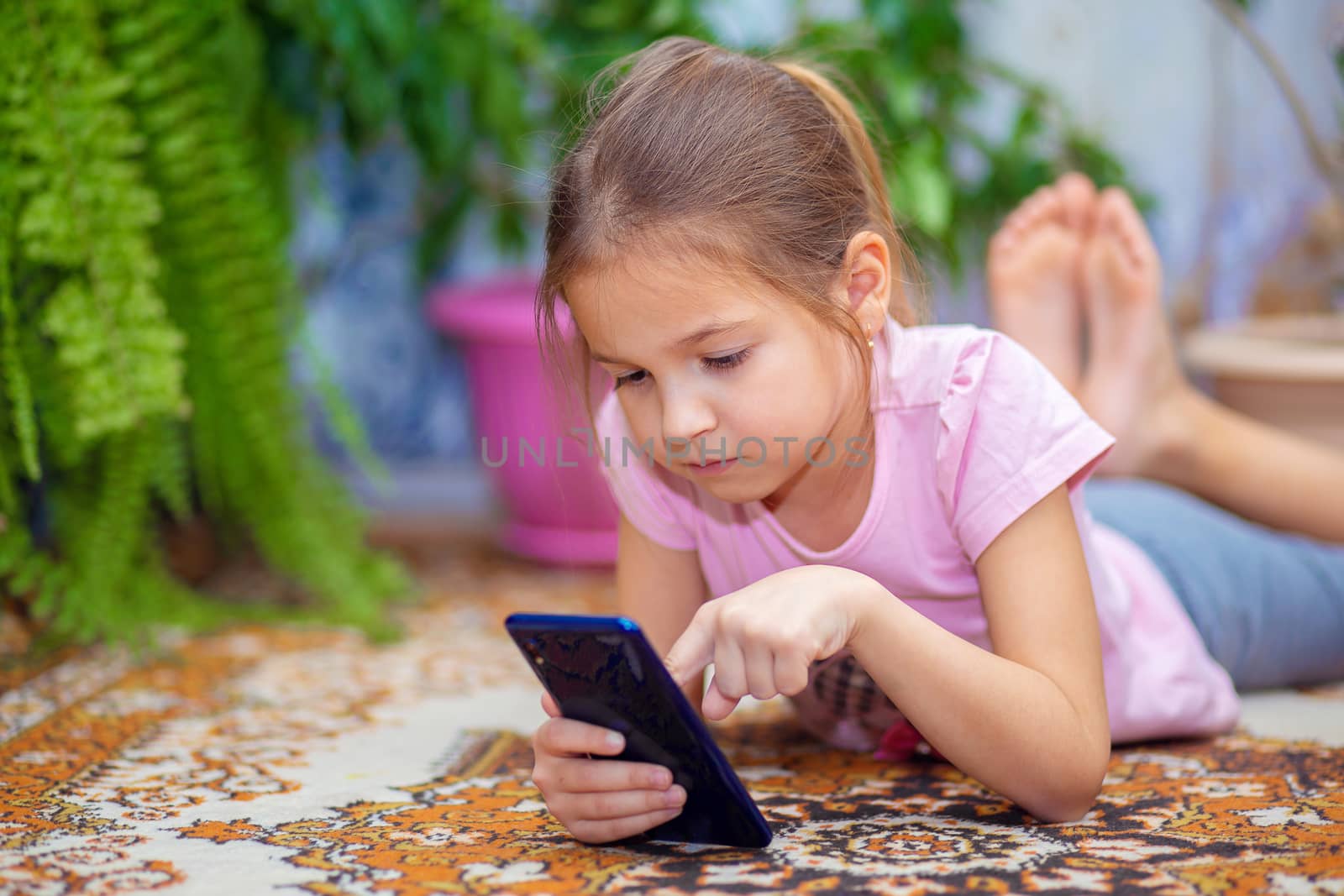 A girl lies on the floor and plays on a smartphone. Child and technology. The child sits at home and has fun with the phone.