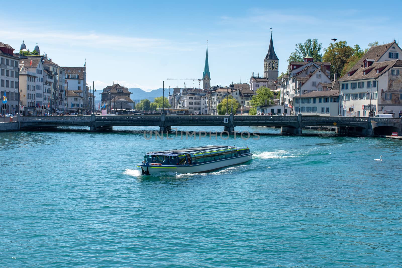 Boat crosses the river in downtown Zurich, Switzerland with cathedrals, old historic buildings in background.