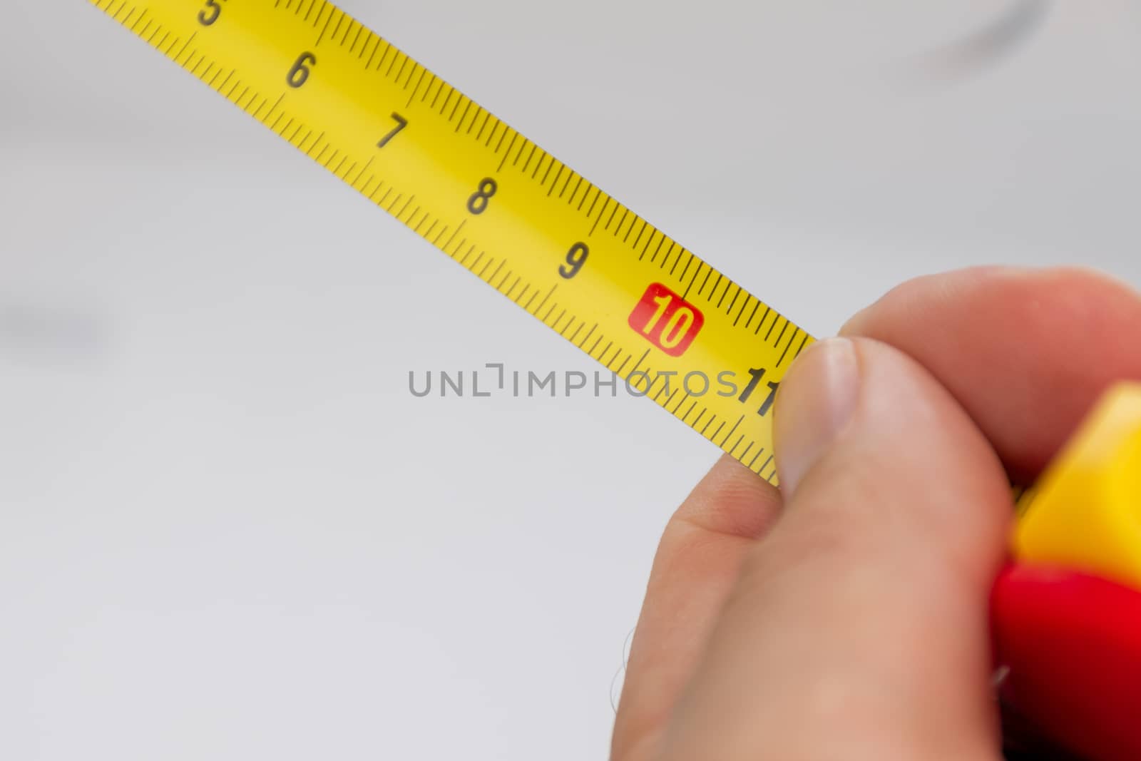 A close up of a yellow metric tape measure with a white hand holding it close for precision.