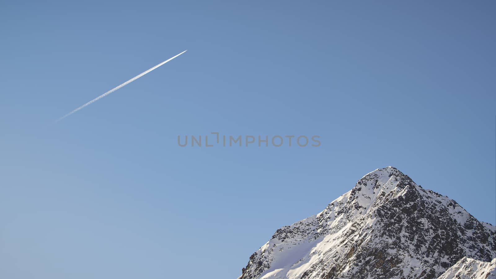 Plane flying with blue skies in a sunny day above a mountain peak of Austrian Alps during winter