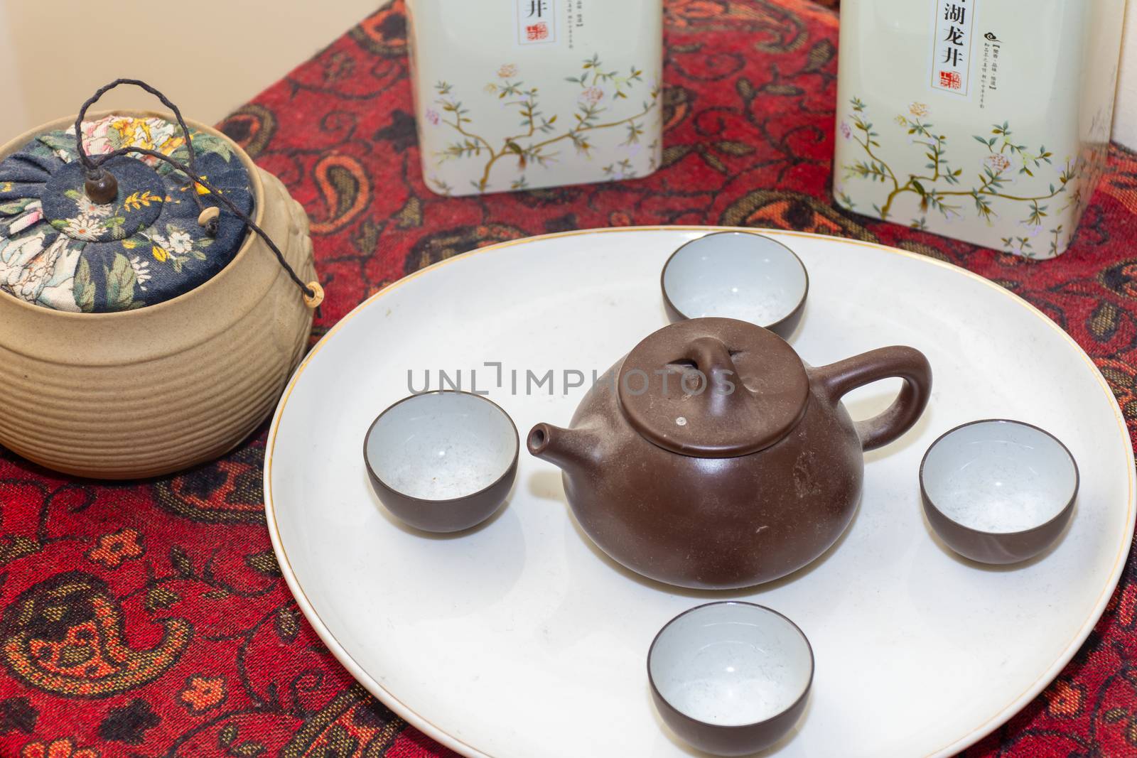 Brown clay Chinese tea set spread out on a white plate. next to traditional herbal tea in clay pots and tin cans.