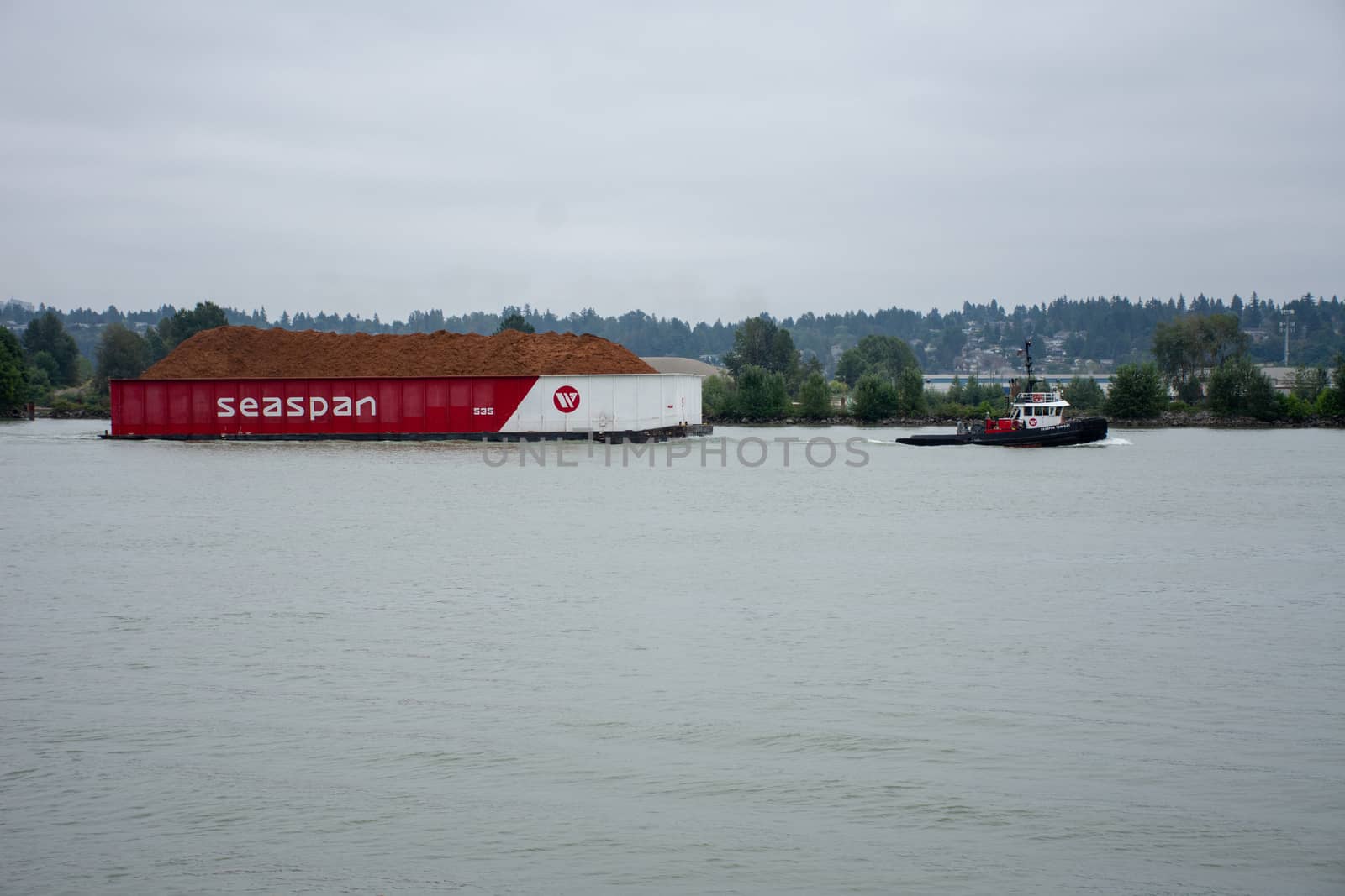 "New Westminster, BC/Canada - 8/2/2018: A Tugboat pulling a Seaspan barge in New Westminster, British Columbia, Canada looking from the Quay in the Fraser River near Surrey."