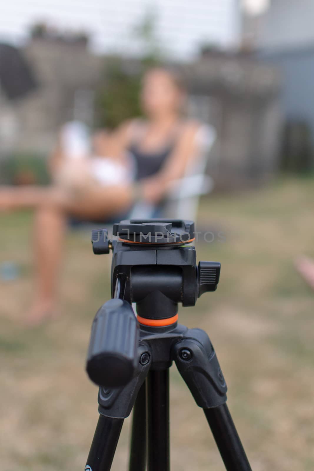 An empty black tripod looking towards a blurred women and child outdoors for a photography shoot. Conceptual.