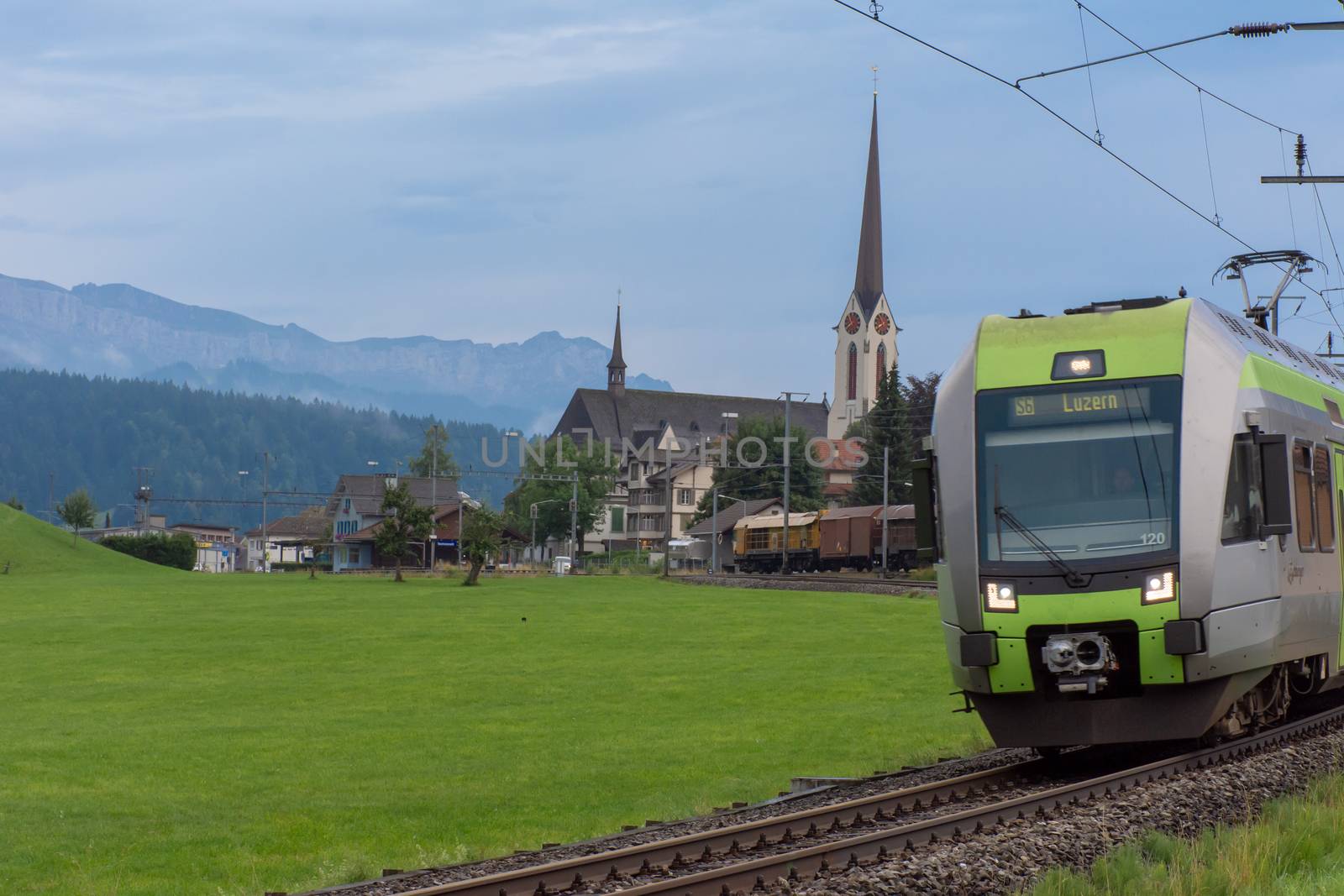"Thun, Thun/Switzerland - 08/11/2018: European passenger train on its way to Luzern, Switzerland passes a small town, cathedral and nearby mountains/Alps.