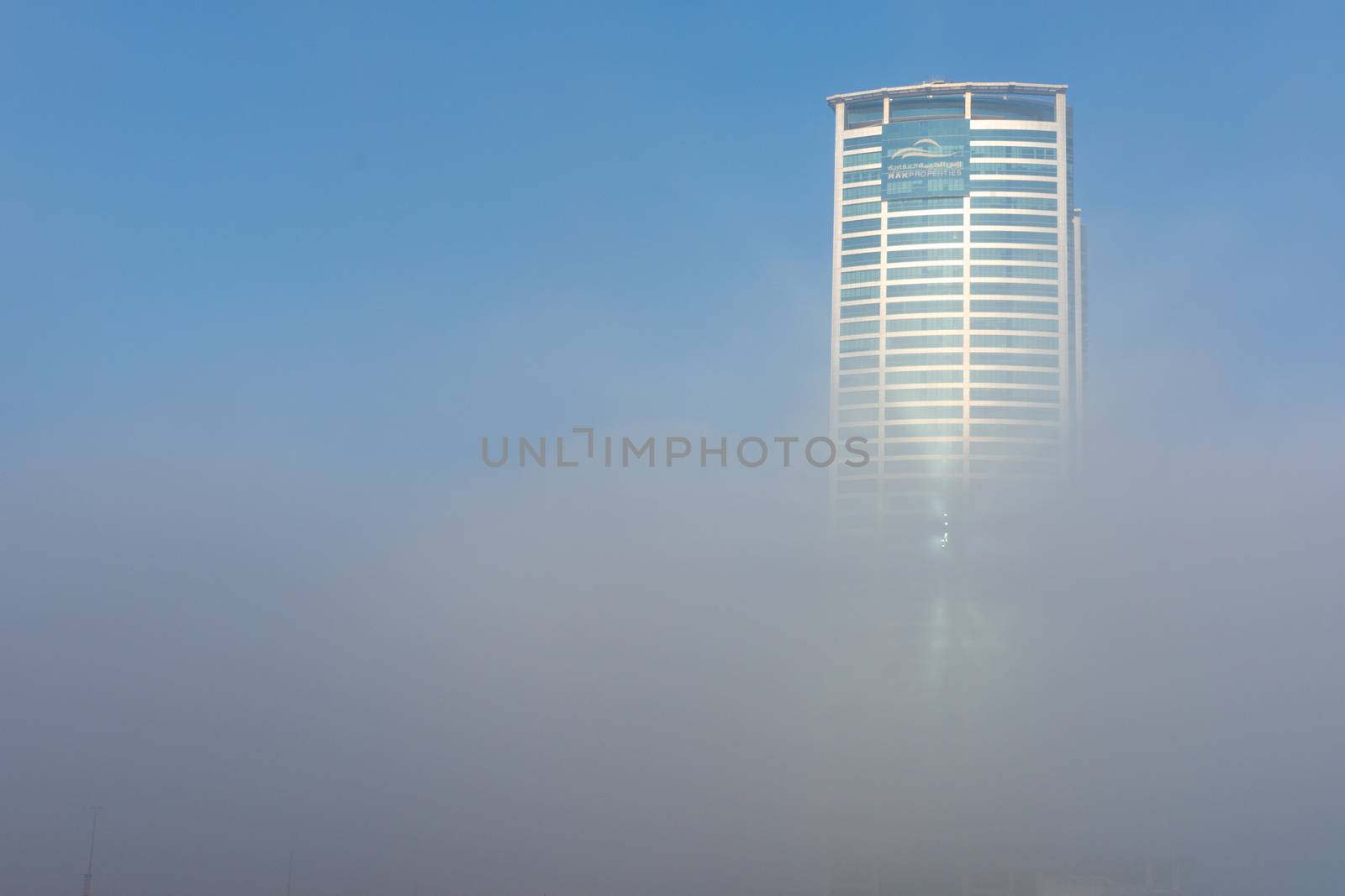 "RAK, RAK/UAE - 10/5/2018 Ras Al Khaimah City in the United Arab Emirates in the early morning fog. Julphur Towers, RAK Properties, peeks above the clouds into the blue sky."
