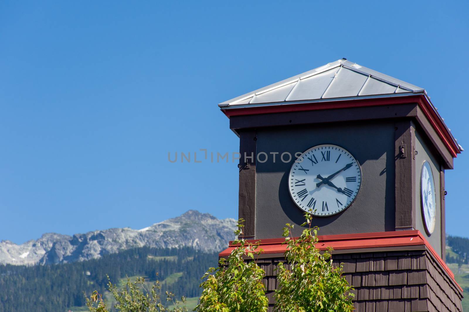 Roman Numeral Clock Tower with rocky mountains and blue sky in t by kingmaphotos