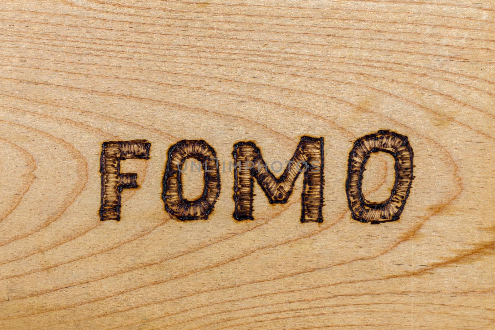 abbreviation FOMO - fear of missing out - burnt by hand on flat wooden surface by z1b
