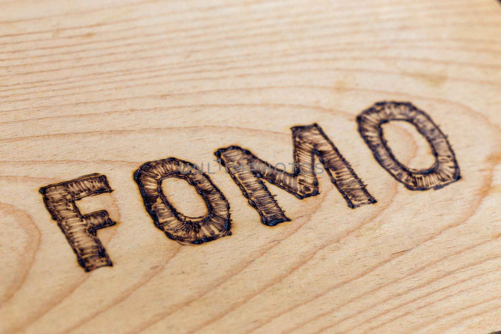 Abbreviation FOMO - fear of missing out - burnt by hand on flat wooden surface. Diagonal close-up view with selective focus.