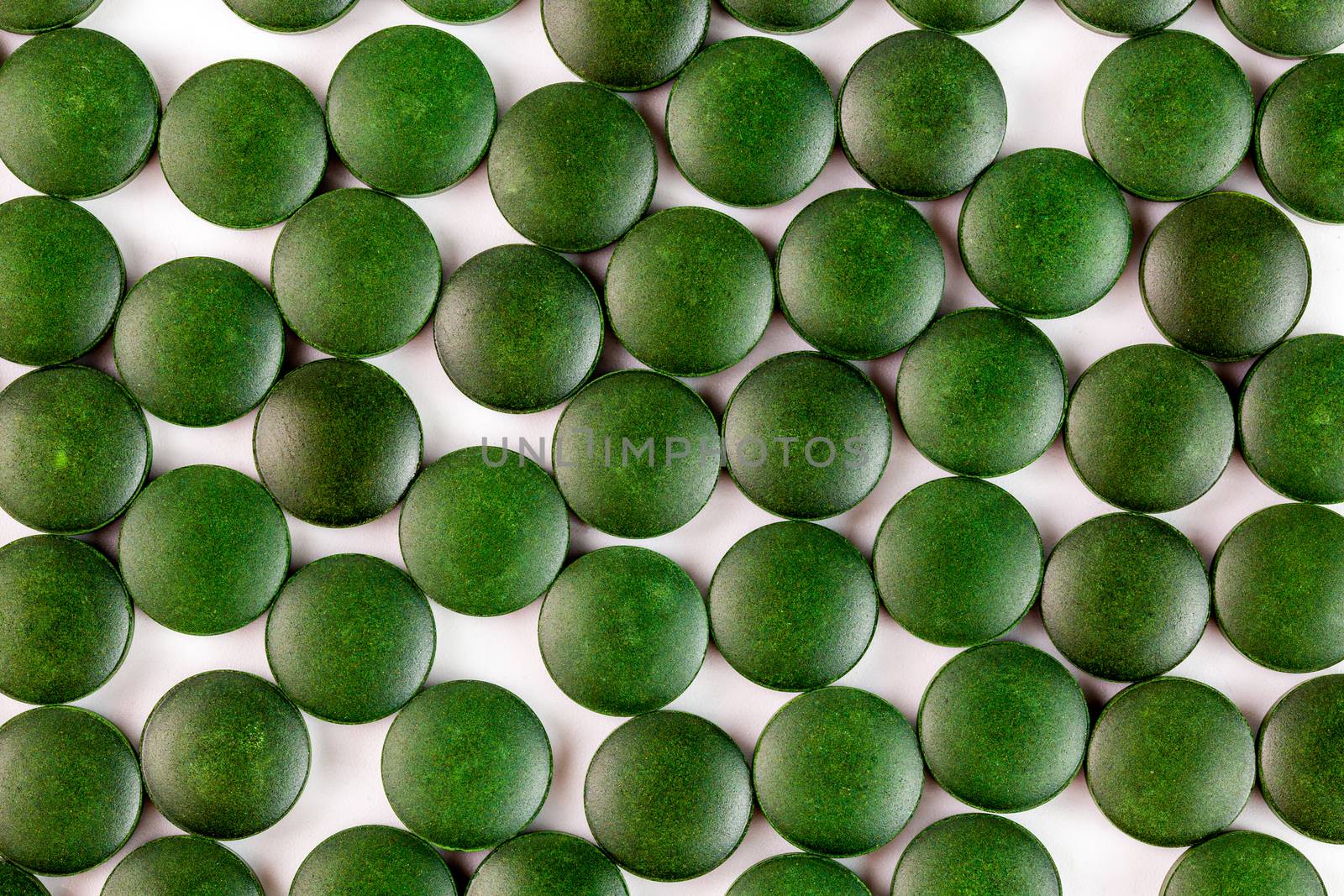 many green organic spirulina tablets laid ramdomly in one layer on flat white surface by z1b