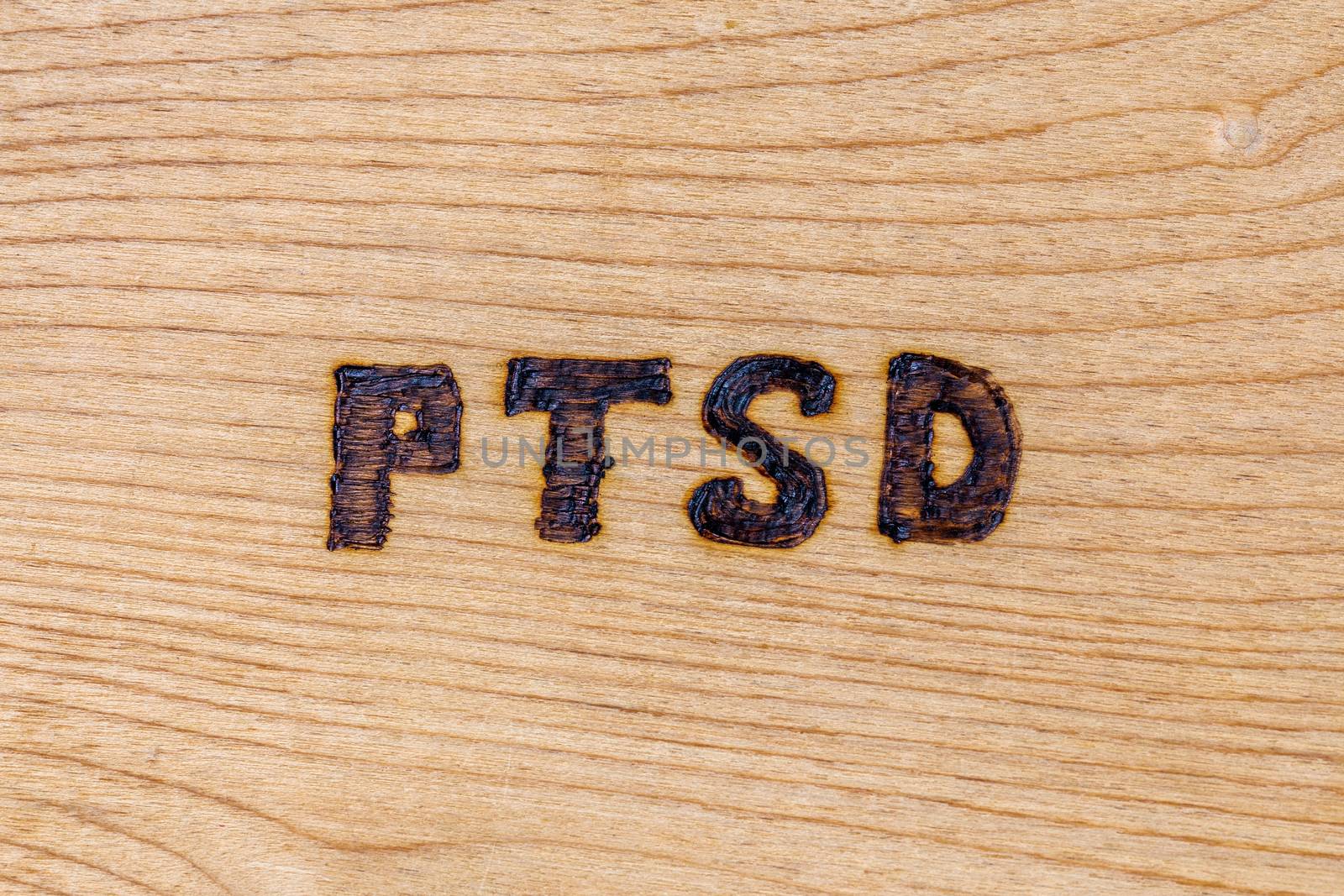an abbreviation PTSD - post traumatic stress disorder - burned by hand on flat wooden board.