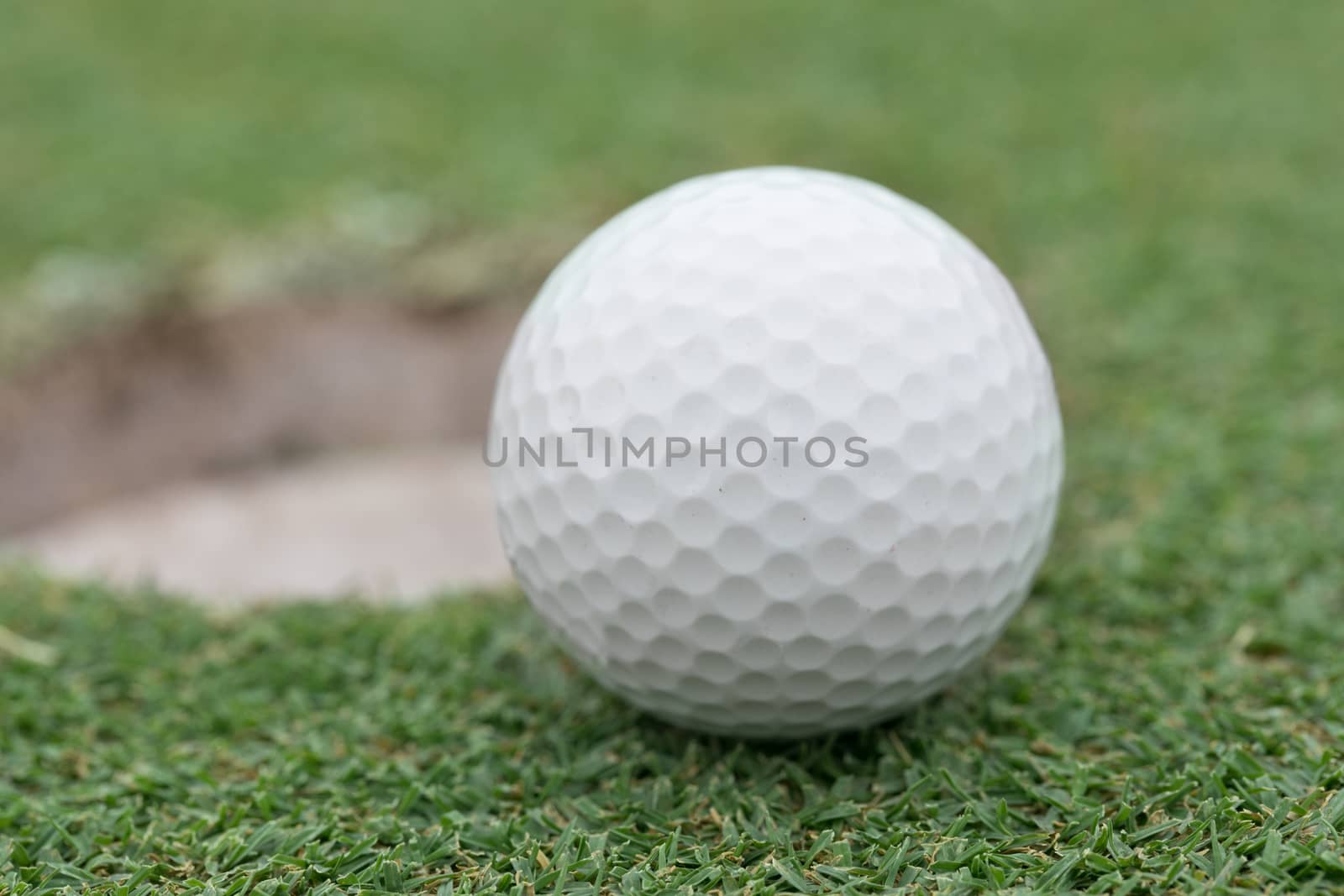 golf ball on lip of cup by Charnsitr