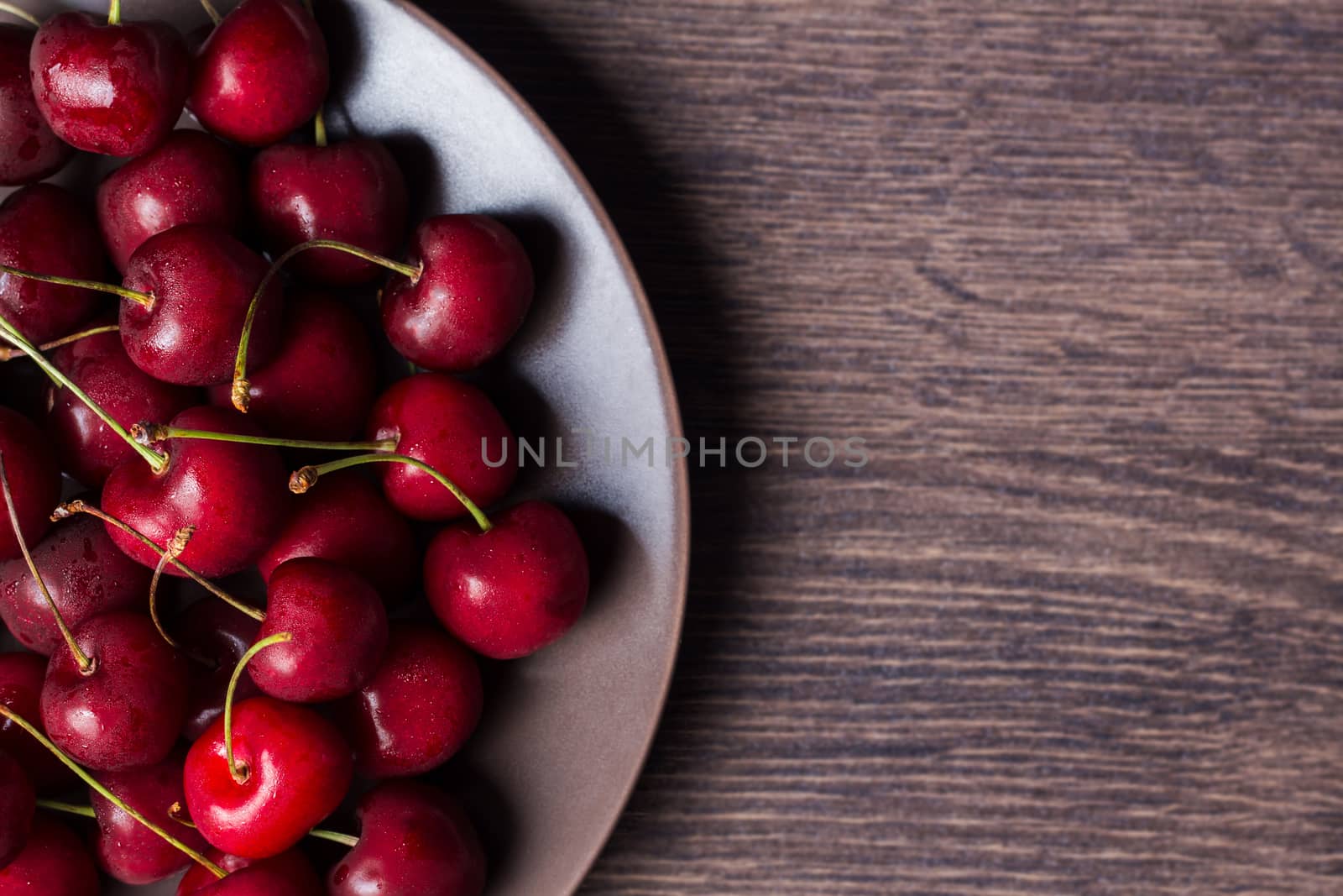 Cherries on a brown plate. Food with copyspace on a wooden table. Berries, snacks, healthy food. Vegan, vegetarian, diabetic, fruit.