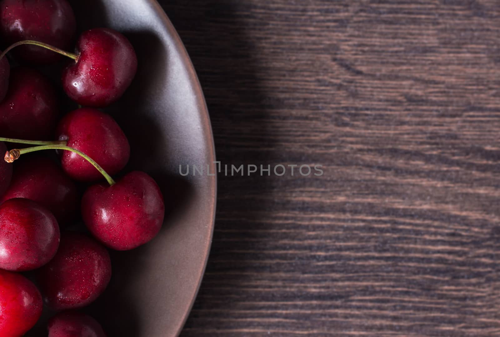 Cherries on a brown plate. Food with copyspace on a wooden table. Berries, snacks, healthy food. Vegan, vegetarian, diabetic, fruit.