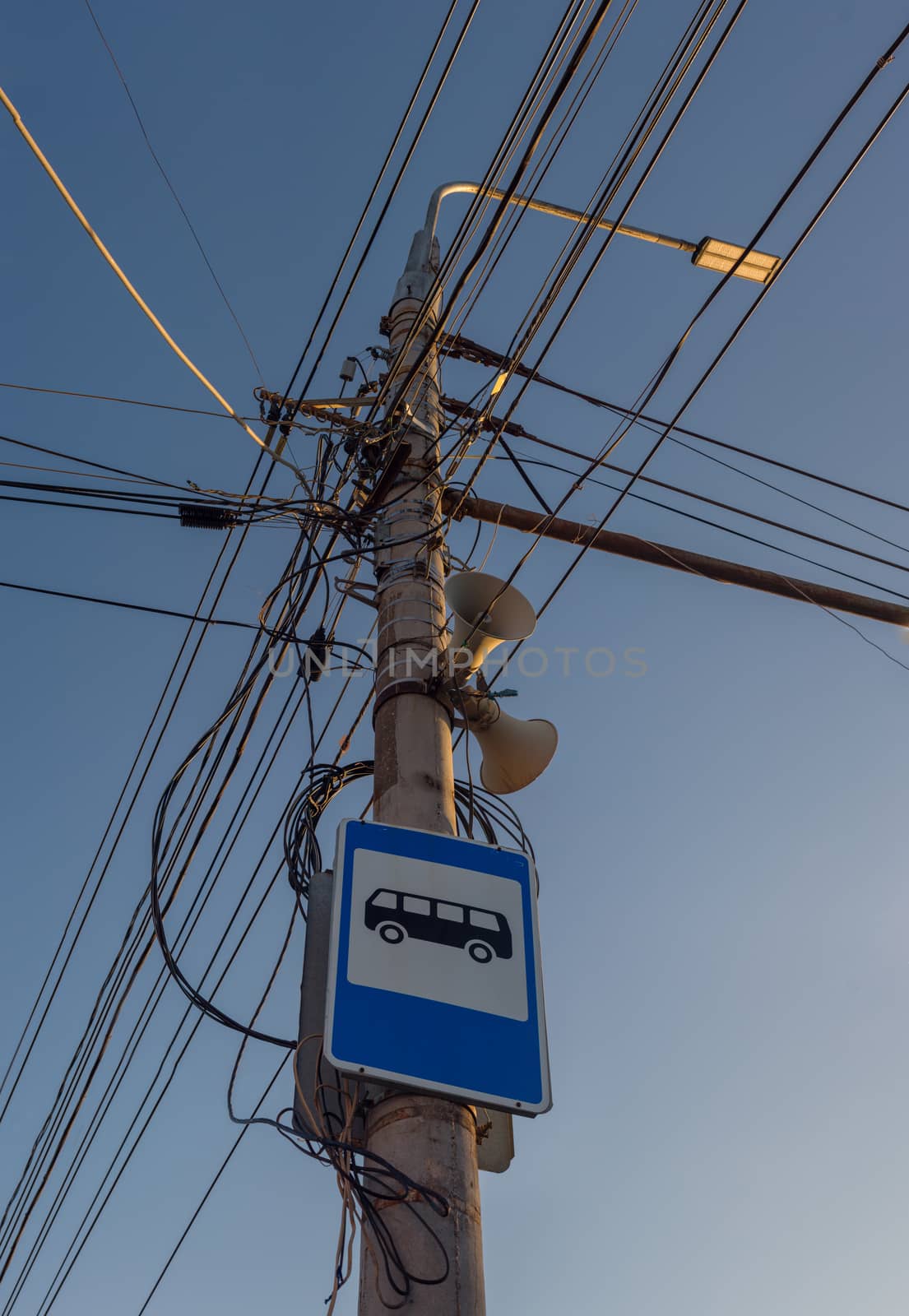 Russian lamp post with a lot of wires, loudspeaker and bus stop sign on blue sky background