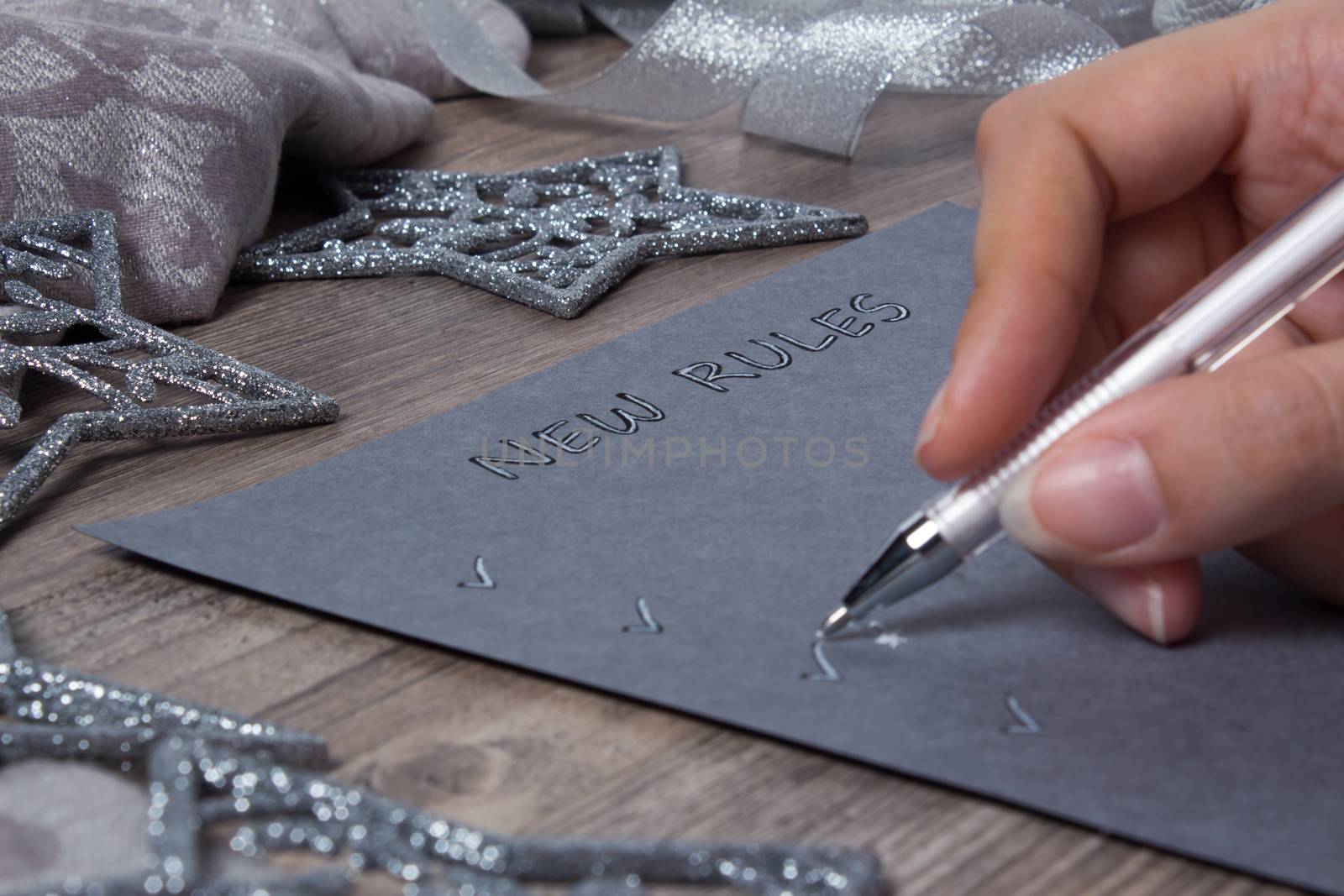 A person writes words on grey paper. New year, new rules. Motivation, plan, schedule, task, new life. Christmas, holiday. Snowflakes and Christmas toys. The silver background.