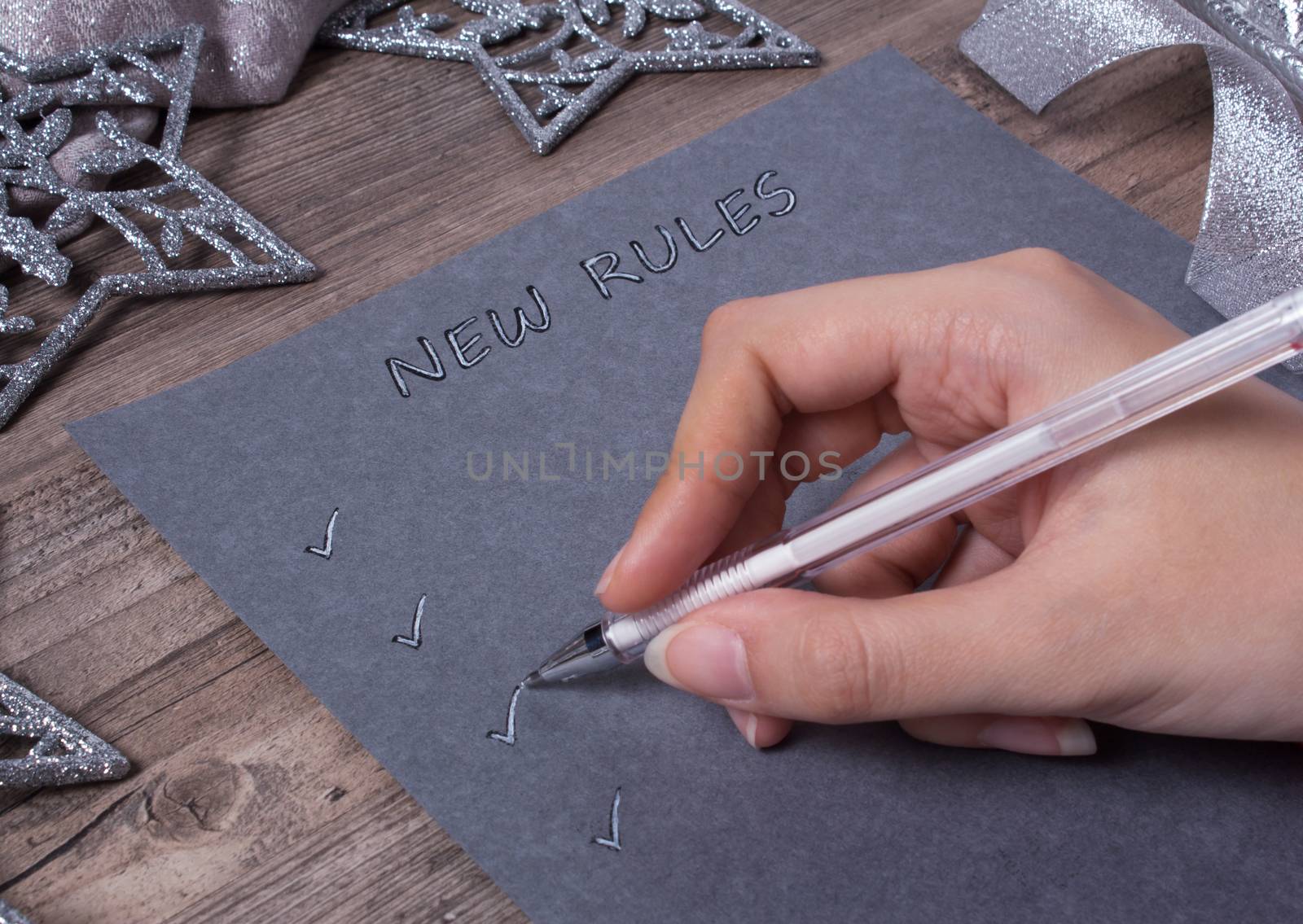 A person writes words on grey paper. New year, new rules. Motivation, plan, schedule, task, new life. Christmas, holiday. Snowflakes and Christmas toys. The silver background.