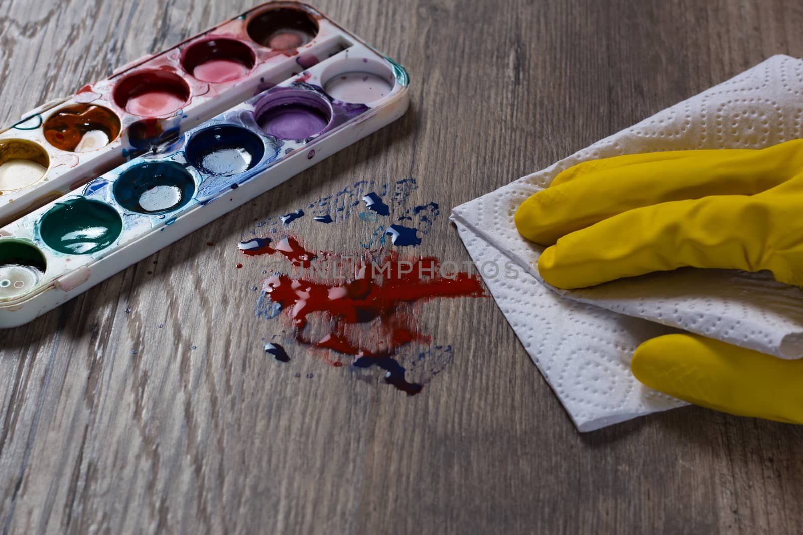 A hand in a yellow protective glove wipes the stain from the paints with a paper towel, a napkin.The woman does the cleaning. Clean, house, housekeeper, cleanup and housework.