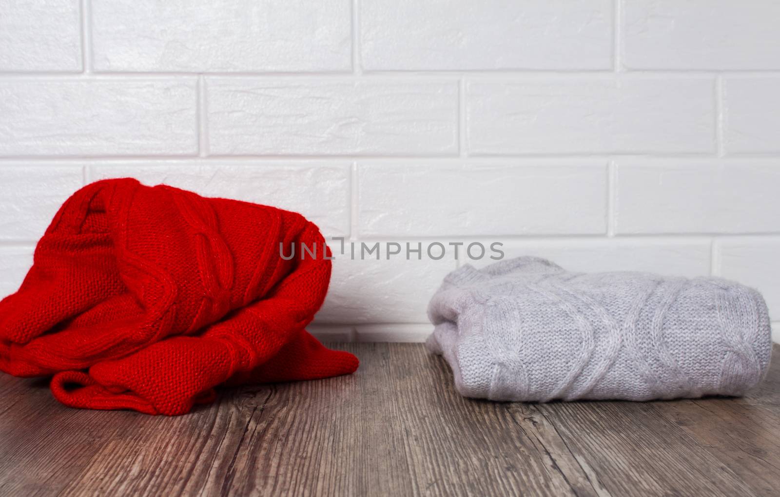 Clothing, fashion, style. Two sweaters on a wooden table. A red rumpled sweater and a melange neatly folded sweater. Order and chaos. Comfort, cleaning, home routine, storage of things.Hygge, cozy, ca