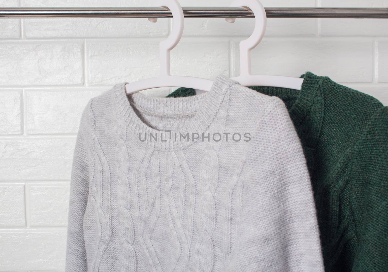 Clothes hang on hangers. Sweaters green and melange colors. Fashion and style, showcase, store, concept. White brick wall, comfort and cleaning, design, hygge, soft and knitwear. Wardrobe.