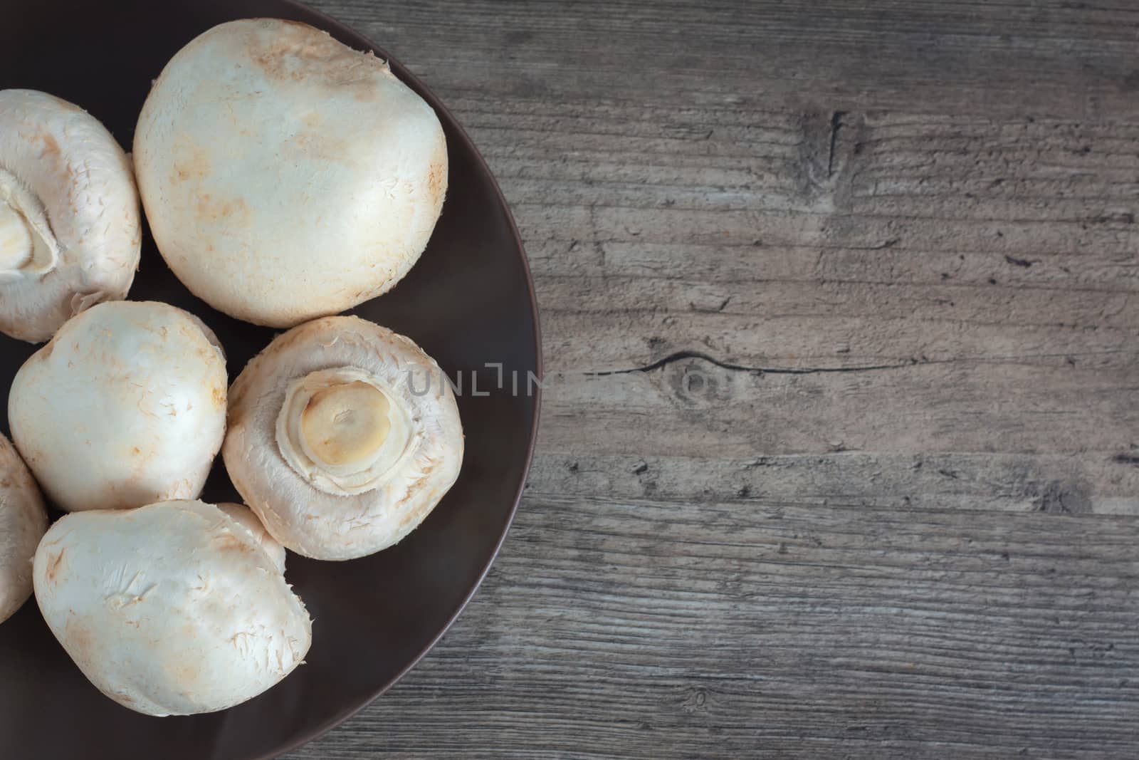 Mushrooms close-up on a wooden table. Champignon on a brown plate. Dietary, vegan, vegetarian, diabetic. Ingredients, recipes. Food, cooking, food. Copy space, clear space, top view.