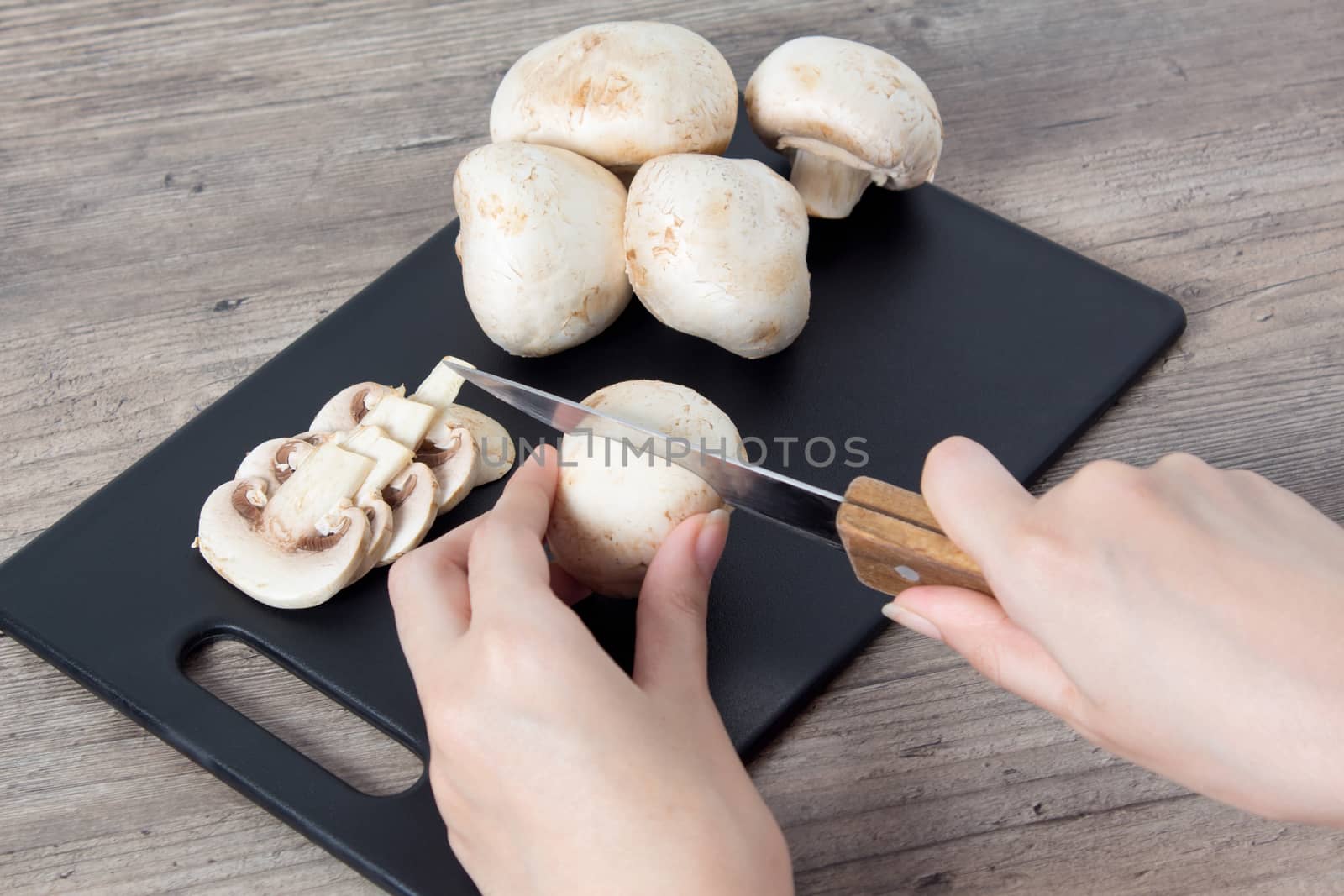 Food. To cook the champignon. Hand cuts mushrooms with a knife on a black cutting Board. Vegan, vegetarian. Top view, close-up