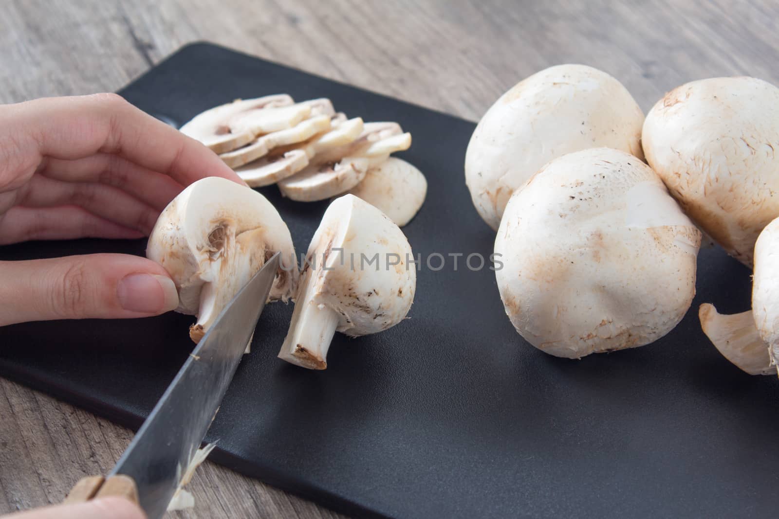 Pieces of champignon mushrooms. The girl cuts mushrooms into halves with a knife. Cooking by a female chef. Top view on a black cutting Board. Food, vegan, vegetarian, dietary.
