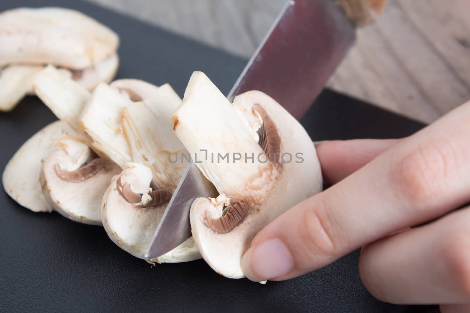 Pieces of champignon mushrooms. The girl cuts the mushrooms into even pieces with a knife. Cooking by a female chef. Top view on a black cutting Board. Food, vegan, vegetarian, dietary.
