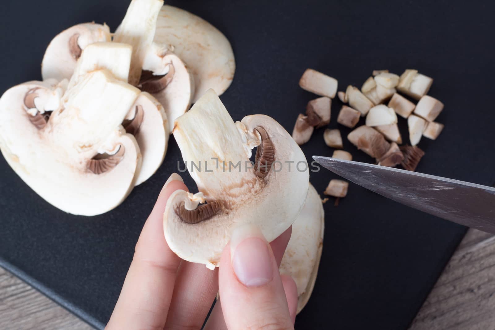 Pieces of champignon mushrooms. The girl cuts the mushrooms into even pieces with a knife. Cooking by a female chef. Top view on a black cutting Board. Food, vegan, vegetarian, dietary.