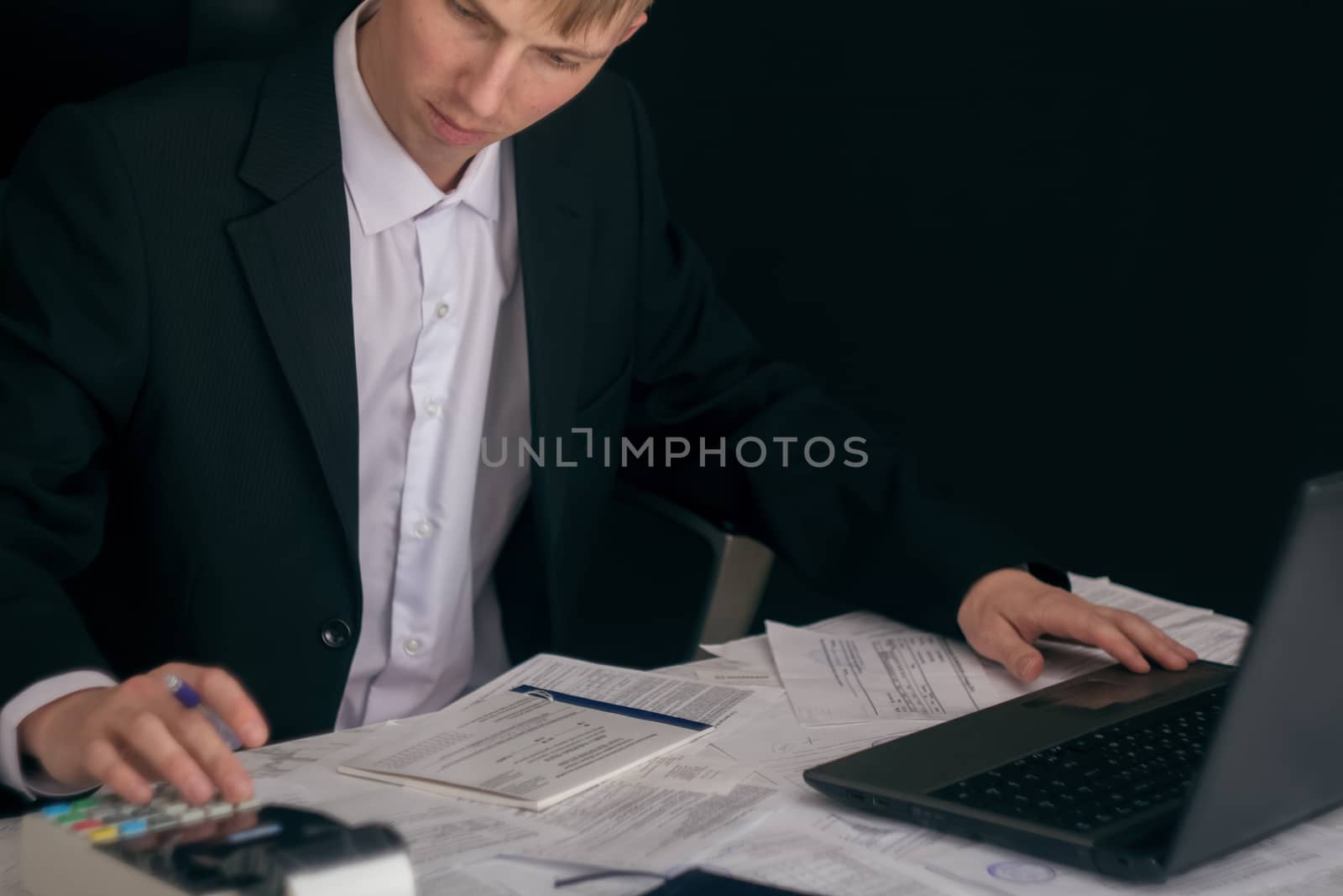 White man working in an office with documents. The Manager makes the report and fills in the Declaration. Businessman at work in his workplace. Young guy at the table with a laptop and cash register.