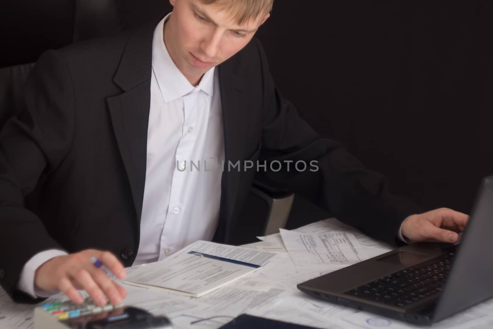 White man working in an office with documents. The Manager makes the report and fills in the Declaration. Businessman at work in his workplace. Young guy at the table with a laptop and cash register.