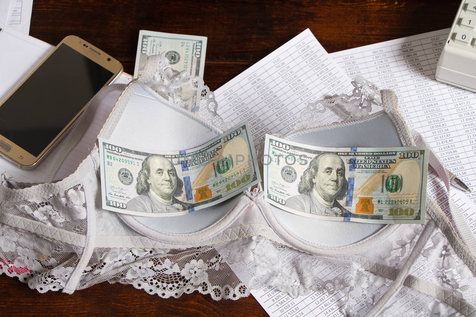A woman's bra with hundred-dollar bills is on the office Desk. brassiere with money on the table. Working in an office or company with documents and financial reports. Love for money in the workplace