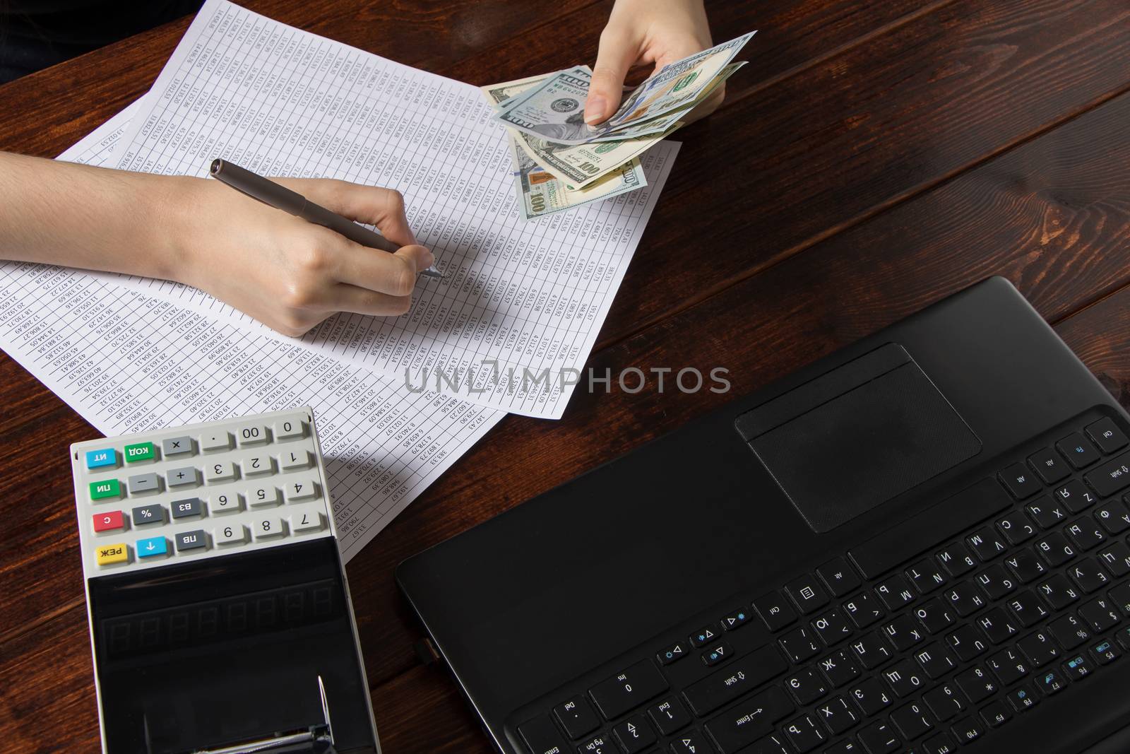 Obligation to pay wages and debts in the company.A cashier holds money dollars over an office work space with documents, a cash register, a phone, and a computer.Work in the office with finances