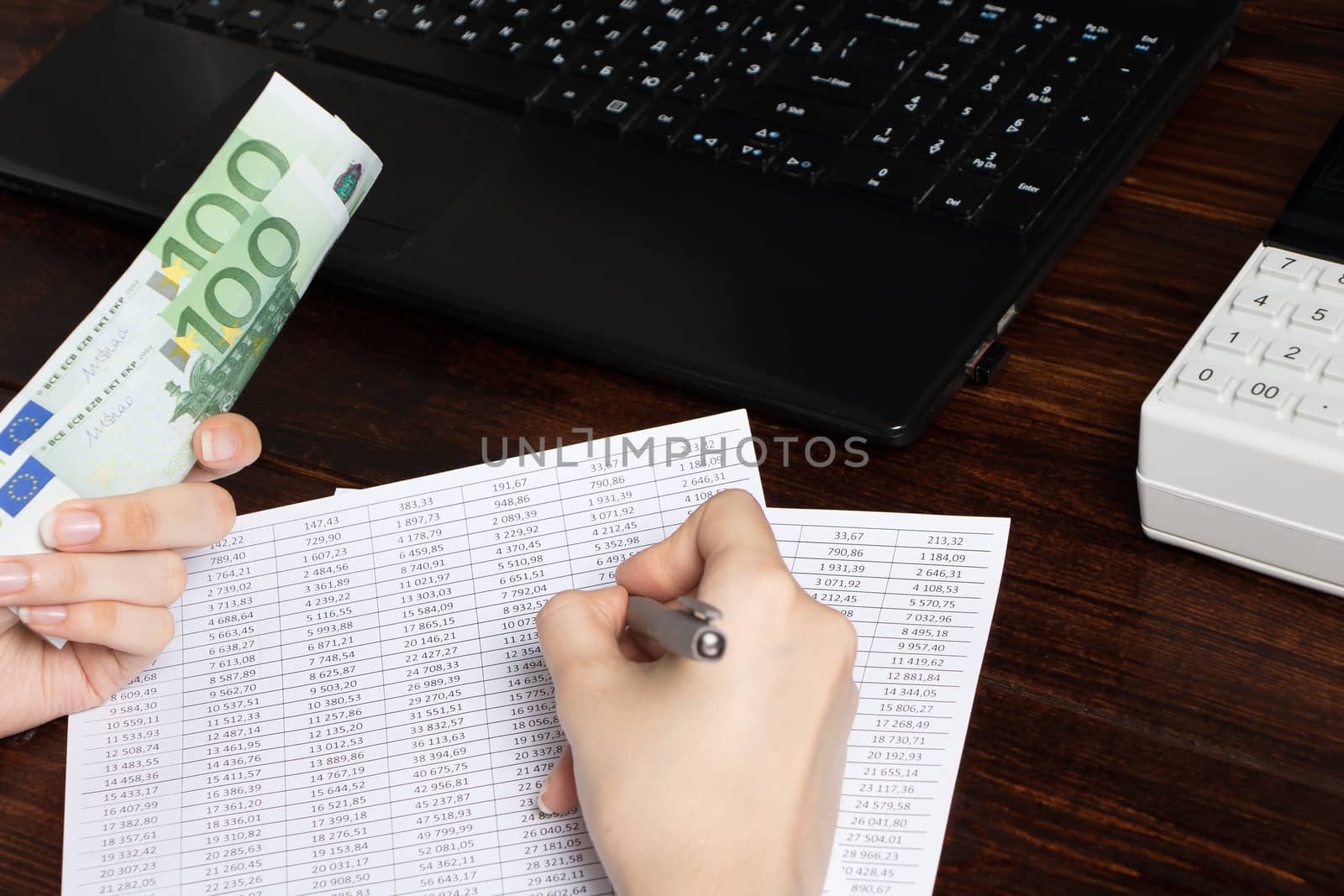 Work in the office with finance. A cashier holds money Euro over an office workspace with documents,a cash register, a phone, and a computer.Obligation to pay wages and debts in the company in Europe