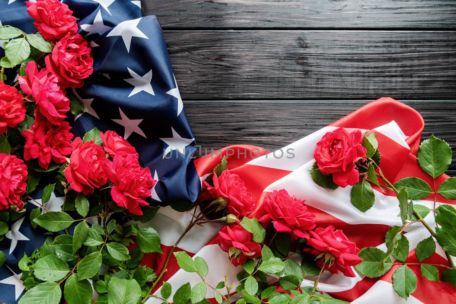 Independence Day USA concept. Memorial Day. Red roses over the USA flag on dark wooden background top view flat lay with copy space