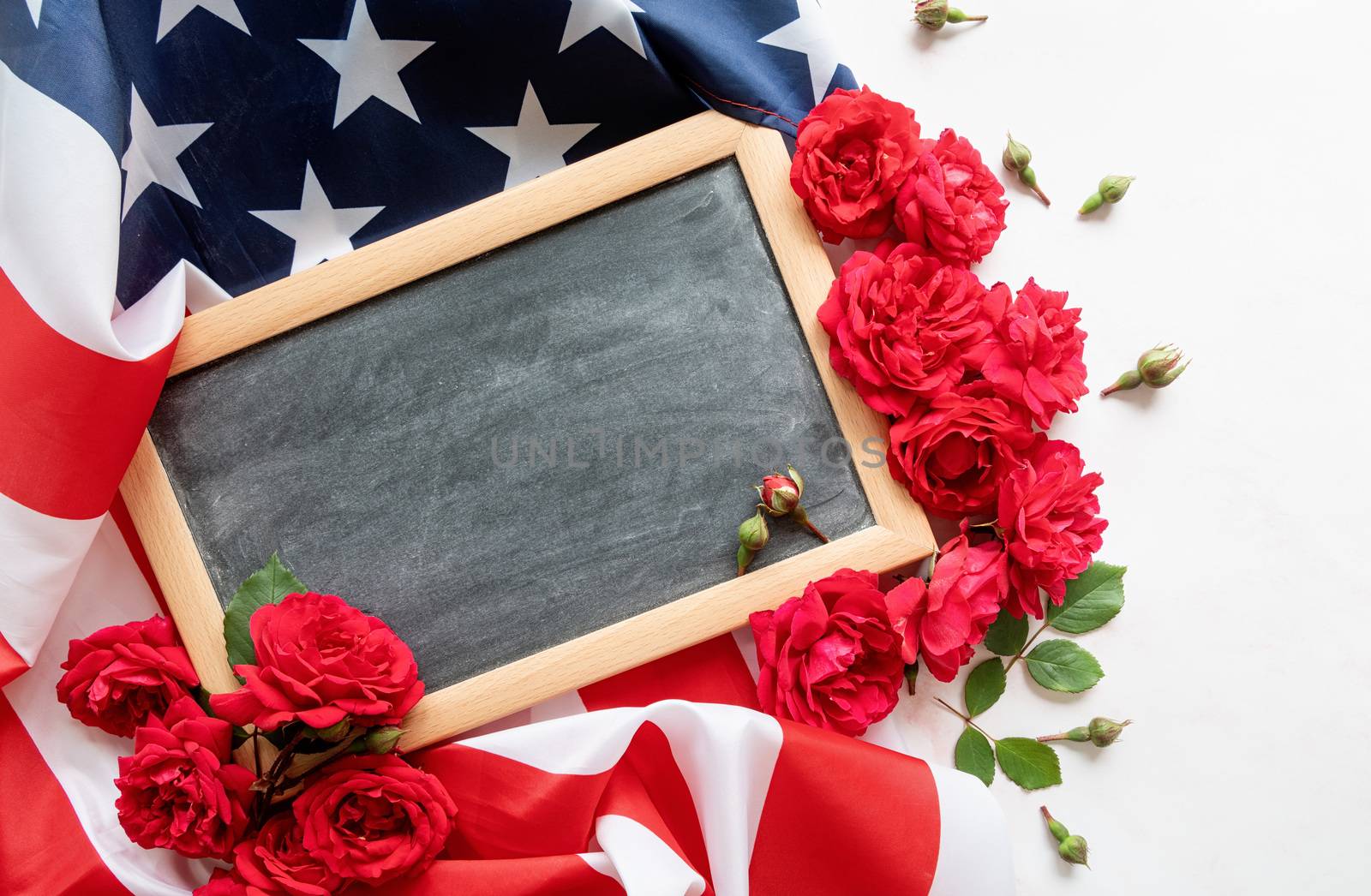 Independence Day USA concept. Memorial Day. Red roses over the USA flag and black letter board top view flat lay