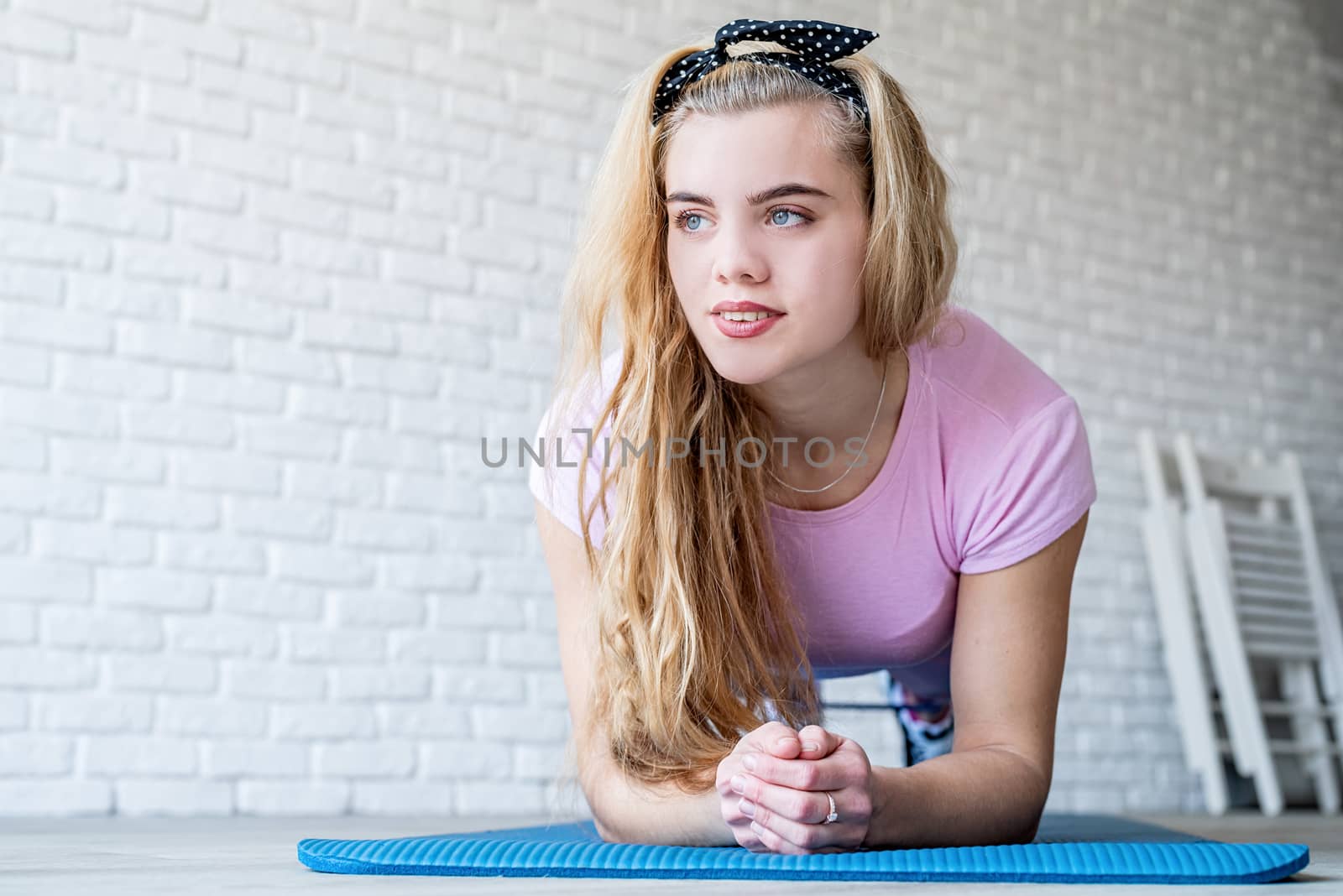 Athletic woman exercising on a fitness mat at home at white brick wall background by Desperada